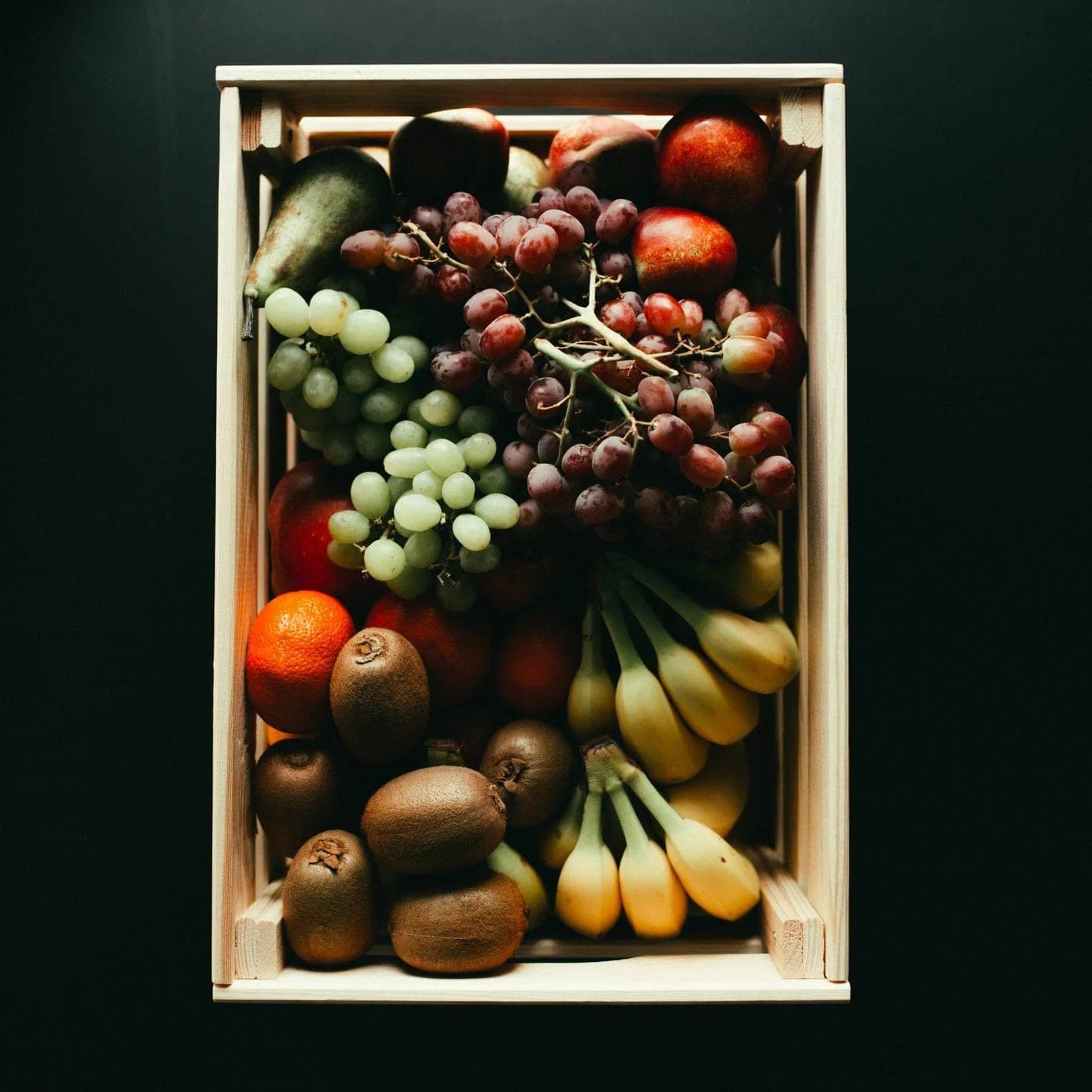Holzkiste von oben: Trauben, Bananen, Kiwis, Äpfel, Orangen und Birnen