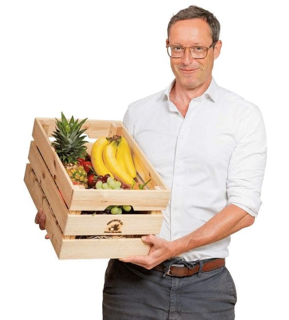 Thomas Müller, Gründer von Obst in dein Büro, mit einer Holzkiste voller Obst
